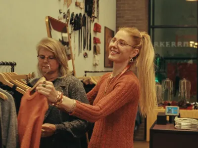 Un·e vendeur·euse aide un·e client·e à choisir un vêtement dans un magasin de prêt-à-porter