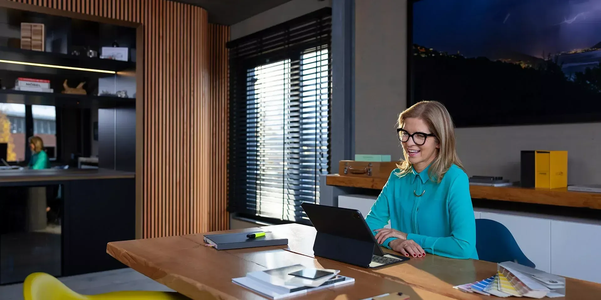 Iemand werkt op een laptop aan een groot houten bureau in een modern kantoor