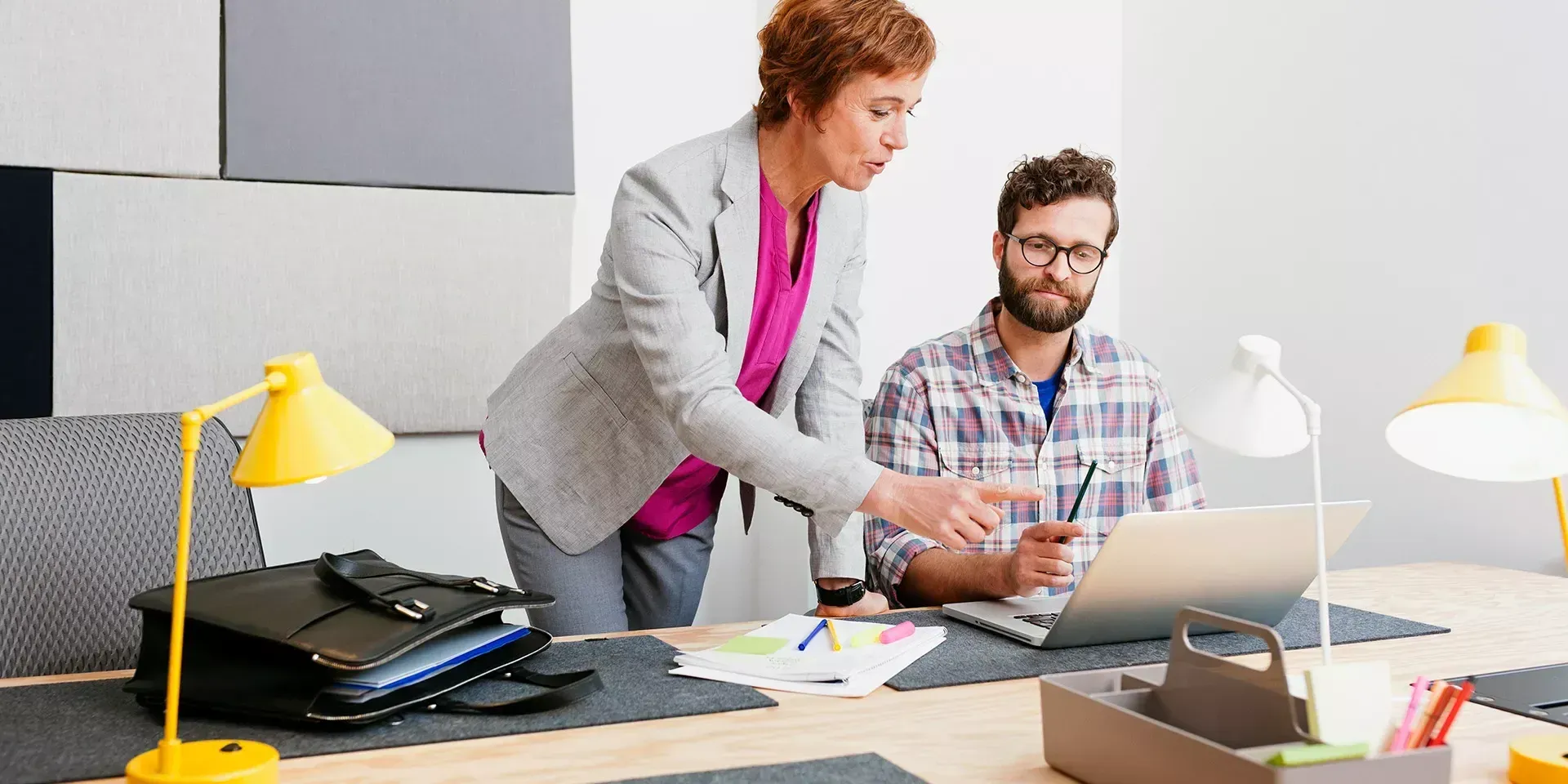 Twee collega's aan een bureau die samen naar een laptop kijken