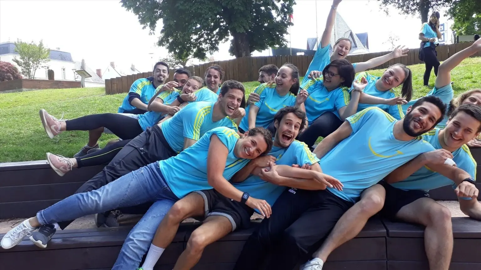Association Siel Bleu team members in matching light-blue t-shirts, piled together laughing on an outdoor bench during a team event.